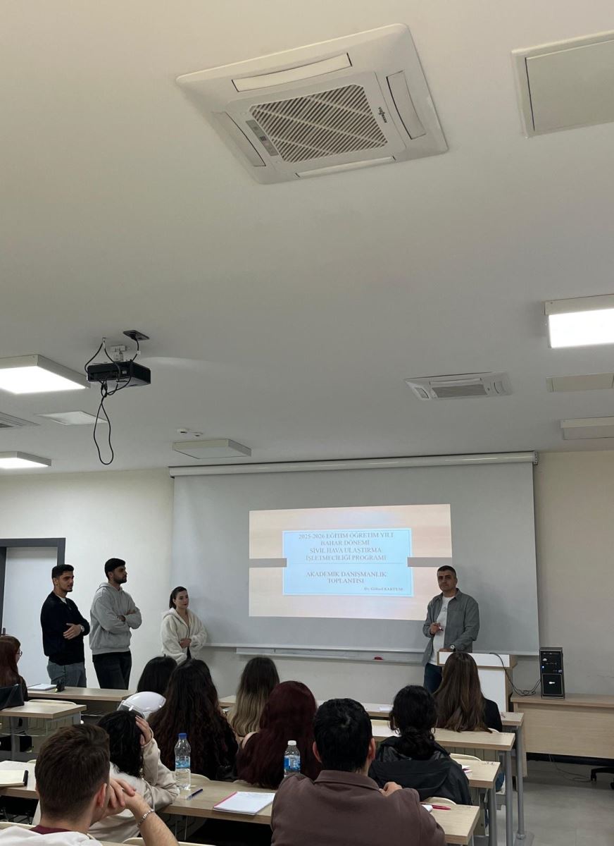 A scene from the academic advising meeting held in a modern lecture hall. The projection screen displays the title "2025-2026 Academic Year Spring Semester Civil Aviation Management Program Academic Advising Meeting." A faculty member is giving a presentation in front of the screen, accompanied by three standing students. In the foreground, students in the front rows are seen from behind, listening attentively.